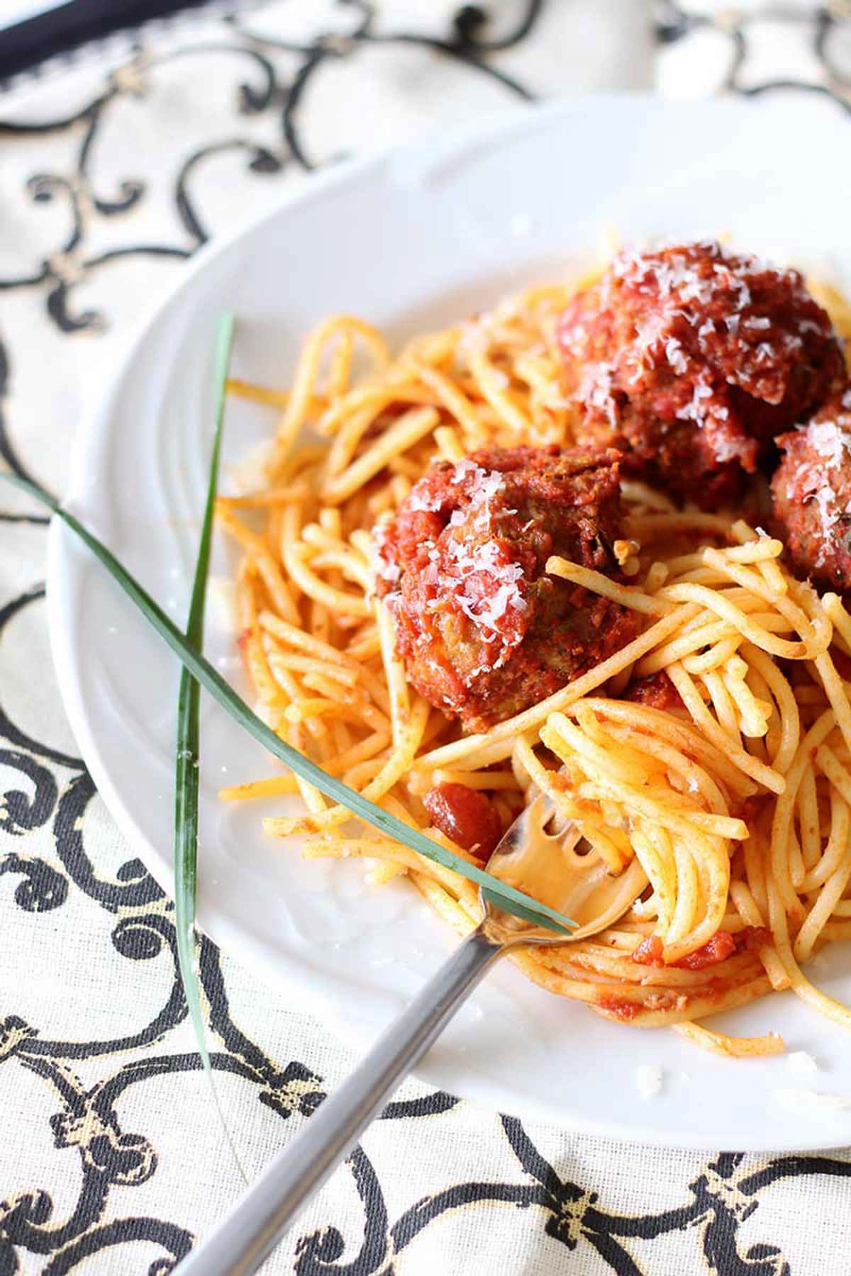 Fork in a plate of pasta with marinara sauce and meatballs. 