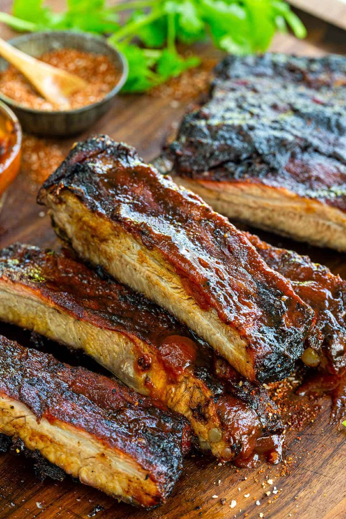 Cut BBQ ribs on a cutting board topped with BBQ sauce. 