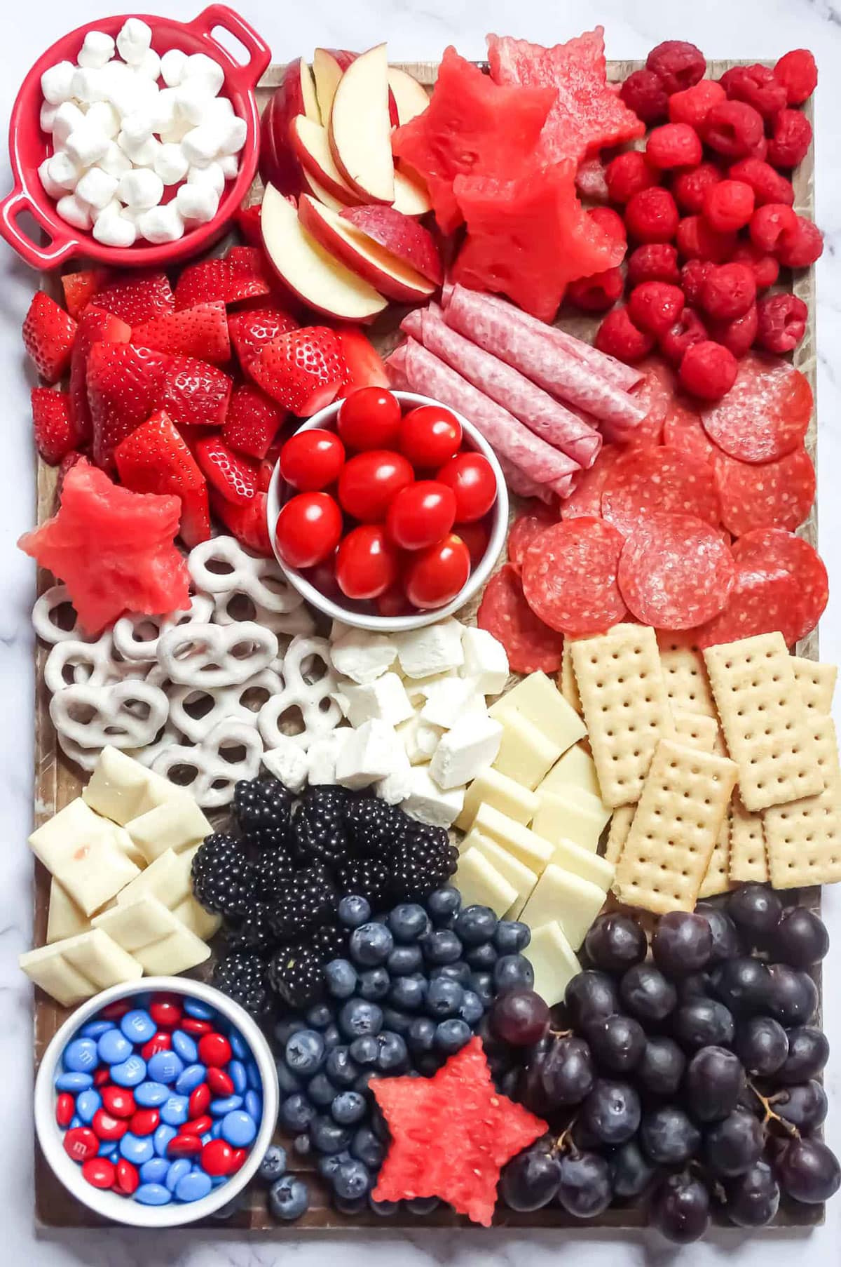 Fruit, pretzels, cheese, crackers, salami, and apples on a board being served as an appetizer. 