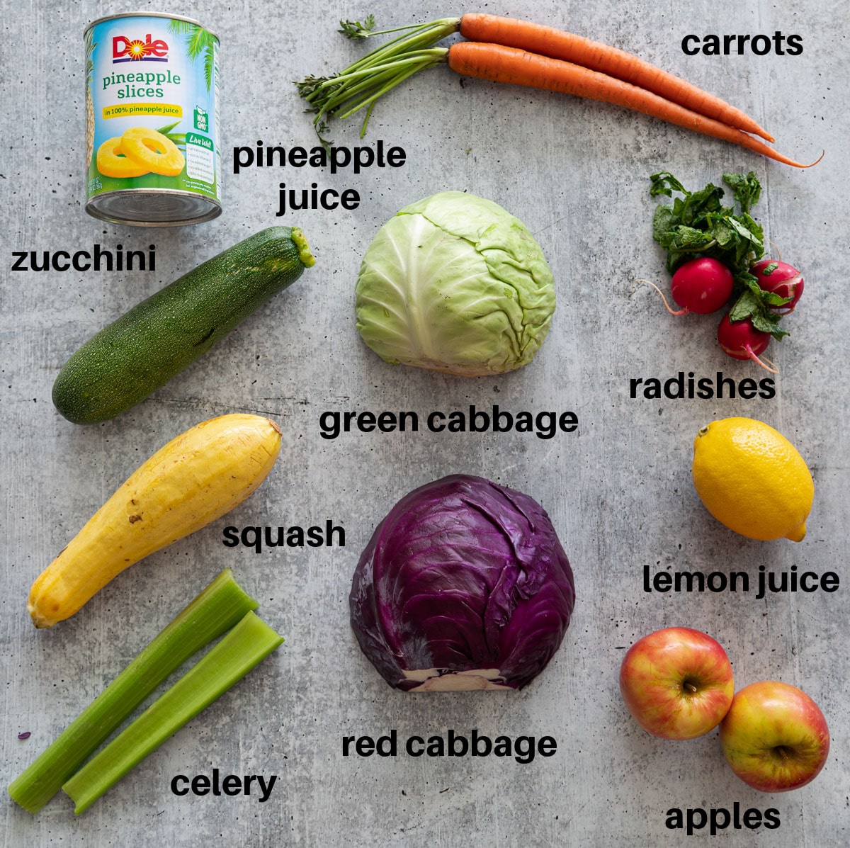 Vegetables in a counter used to make healthy coleslaw: carrots, cabbage, zucchini, squash, celery, radishes, fruit. 