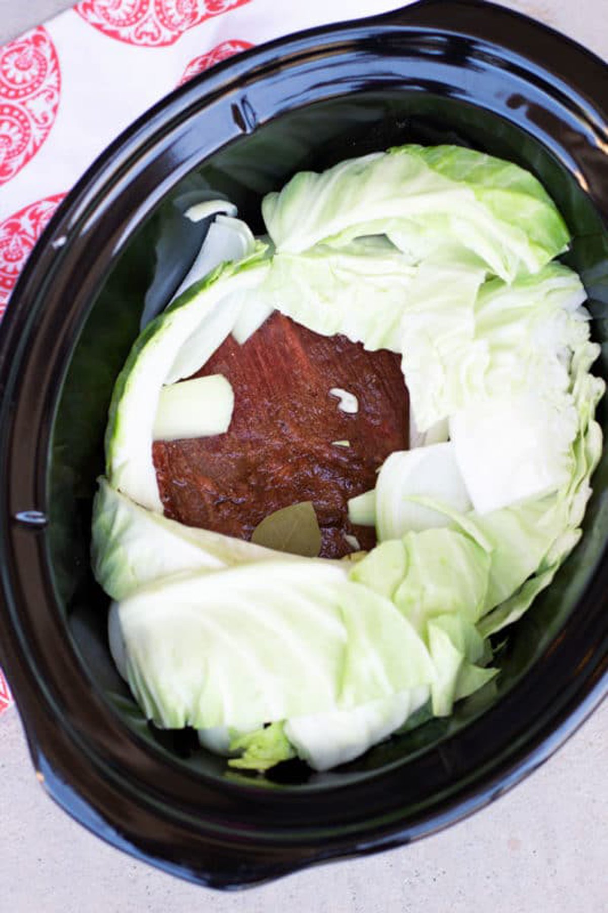 Slow cooked beef brisket in crock pot topped with raw cabbage.