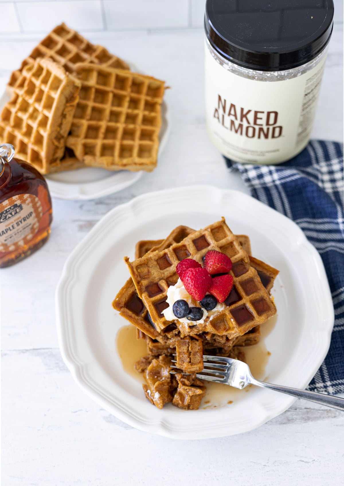 A fork cutting into a plate of pumpkin waffles, topped with butter, syrup, and berries. 