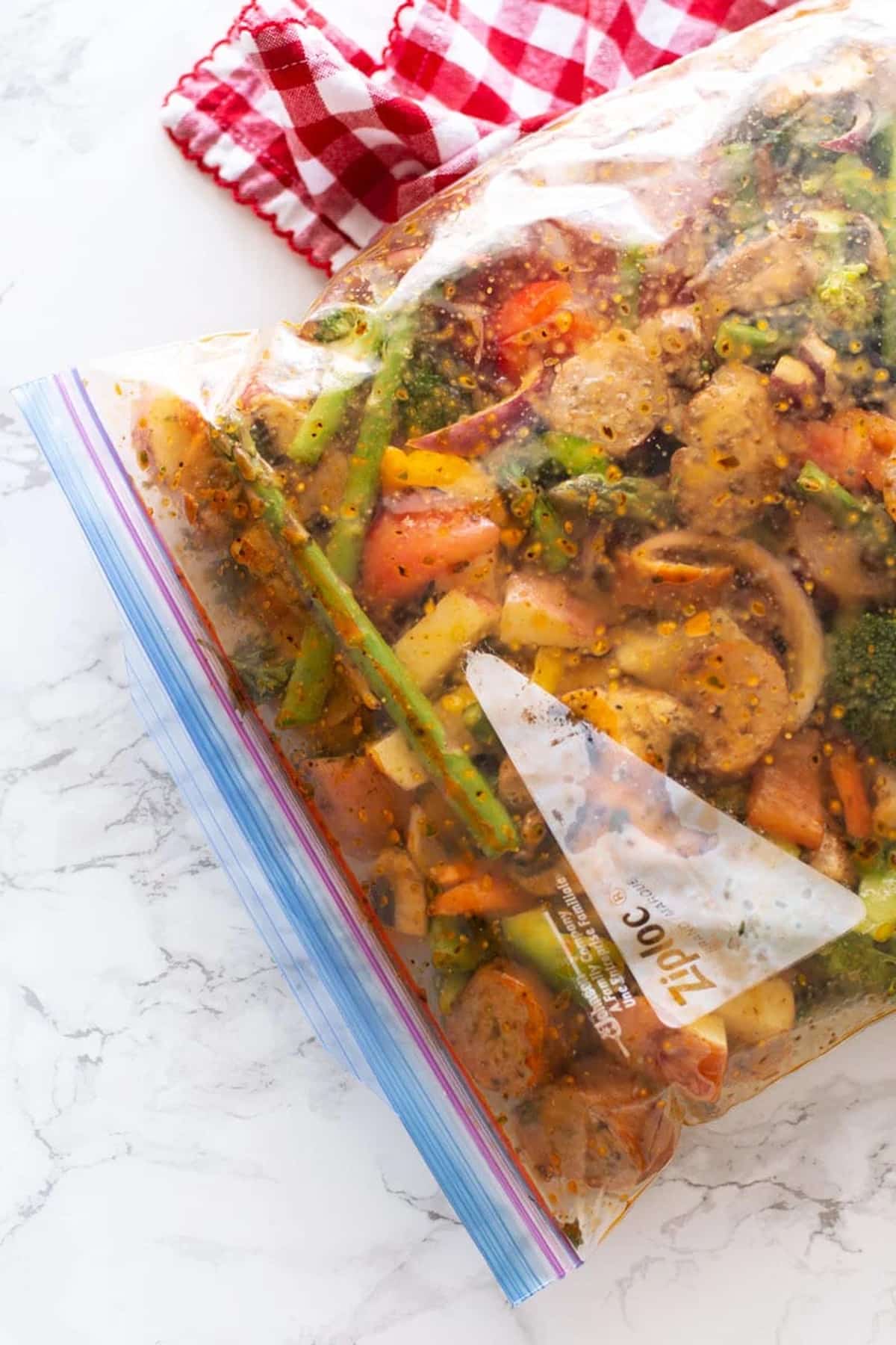 Ziplock bag containing One Pan Smoked Sausage and Vegetables in a lemon herb marinade sitting on white marble counter.