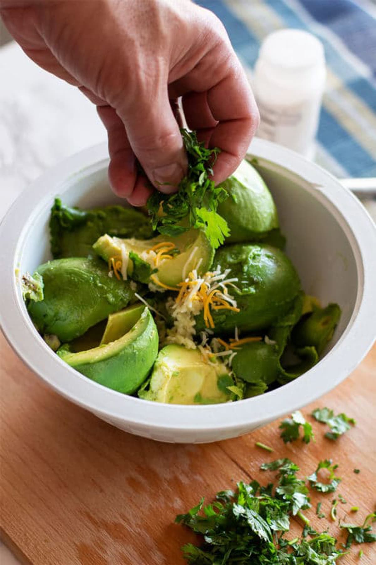 Sprinkling fresh cilantro leaves into the guacamole. 