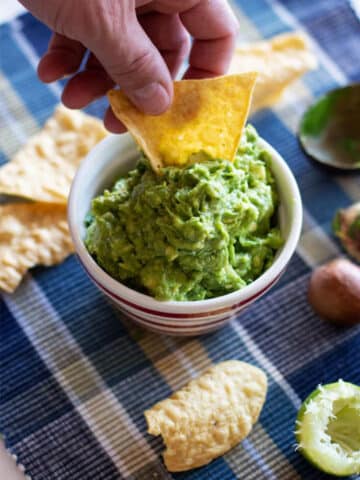 Person dipping chip in bowl of guacamole.
