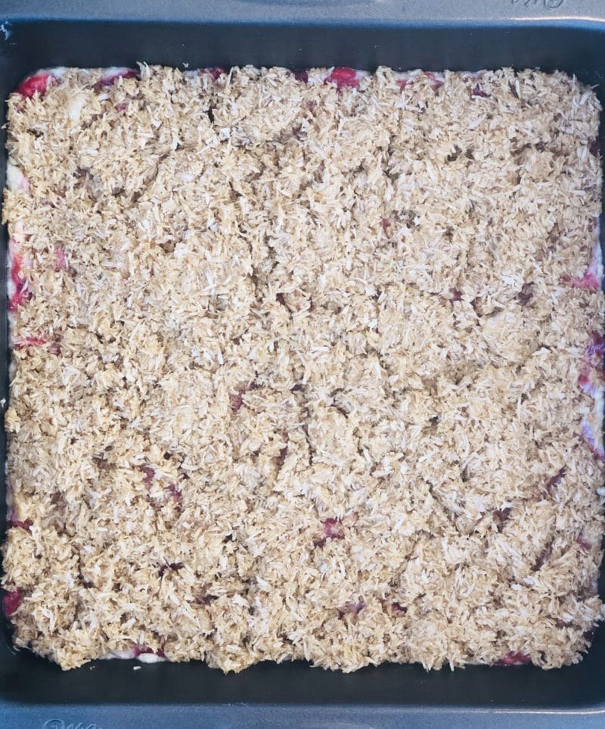 Coconut and sugar spread evenly over raspberry crumble bars before baking.