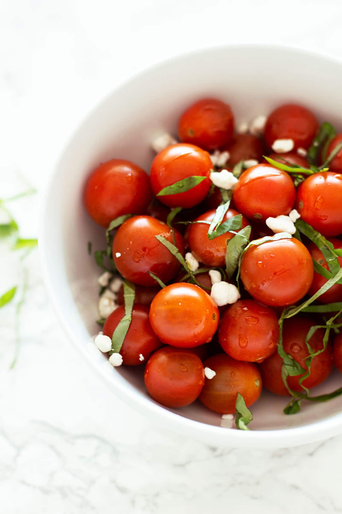 Bowl of raw cherry tomatoes with basil and goat cheese.