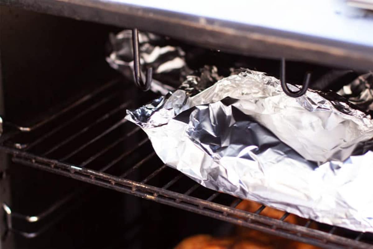 Aluminum foil packet containing cherry tomatoes placed in a smoker.