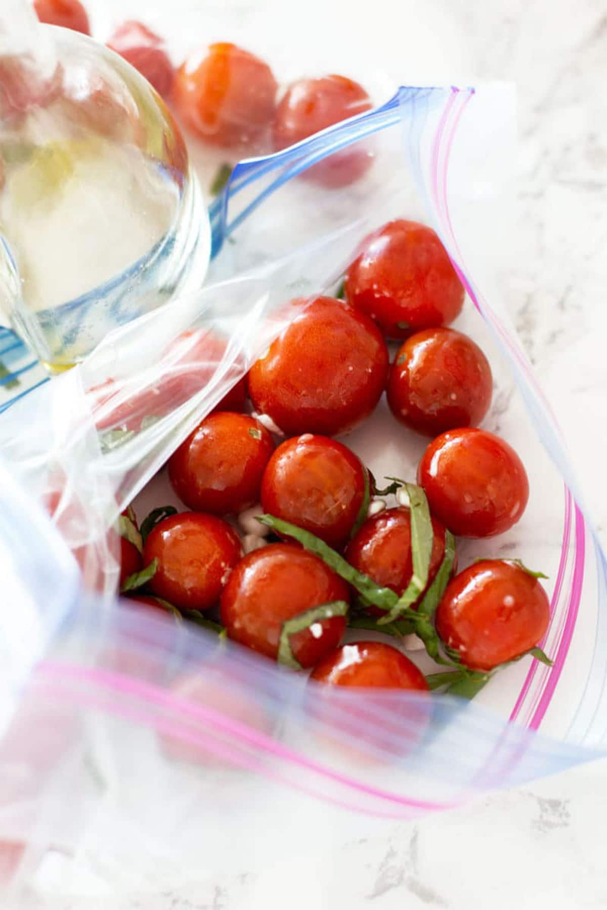 Plastic bag filled with olive oil, basil, and fresh cherry tomatoes.
