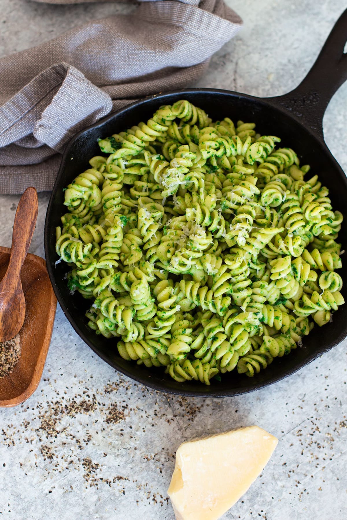 Dish filled with spinach pasta topped with avocado sauce an Parmesan cheese.