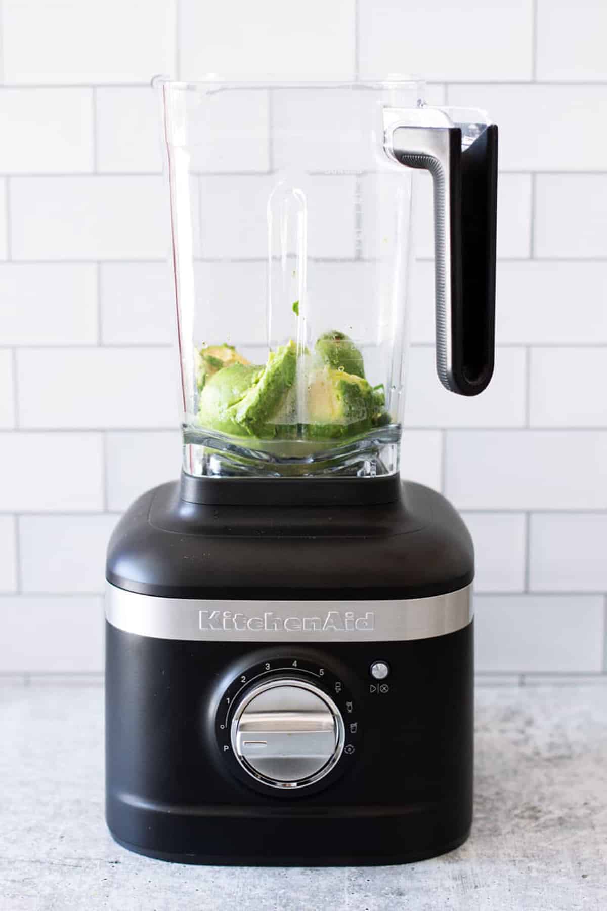 Blender containing chopped avocado and other ingredients to make an avocado sauce. 