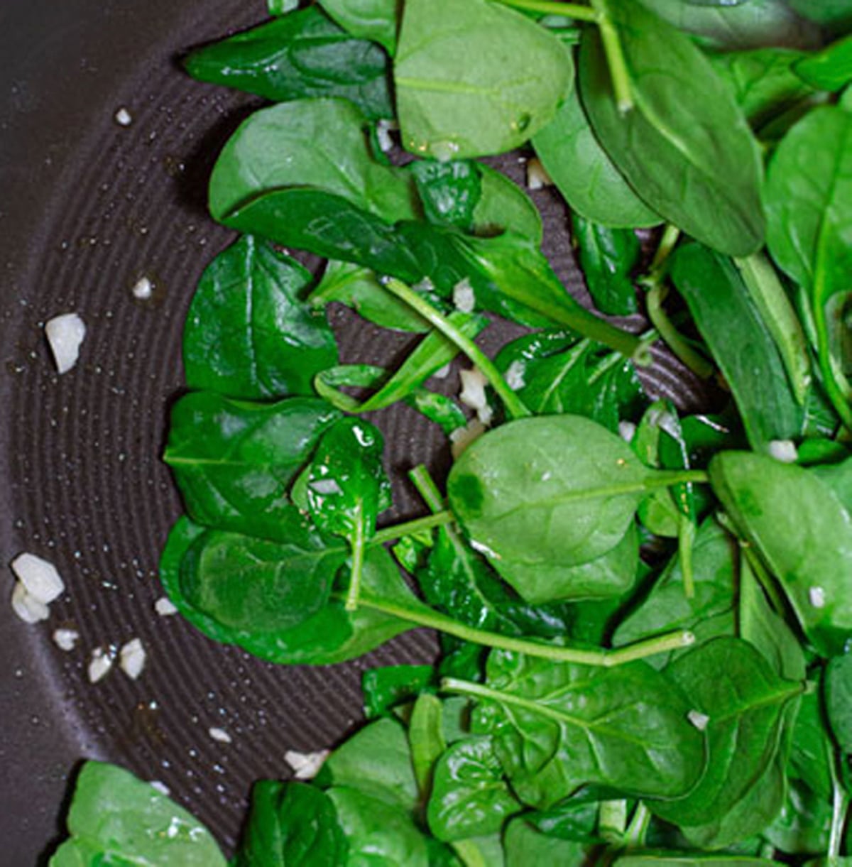 Spinach being cooked in a skillet with minced garlic. 