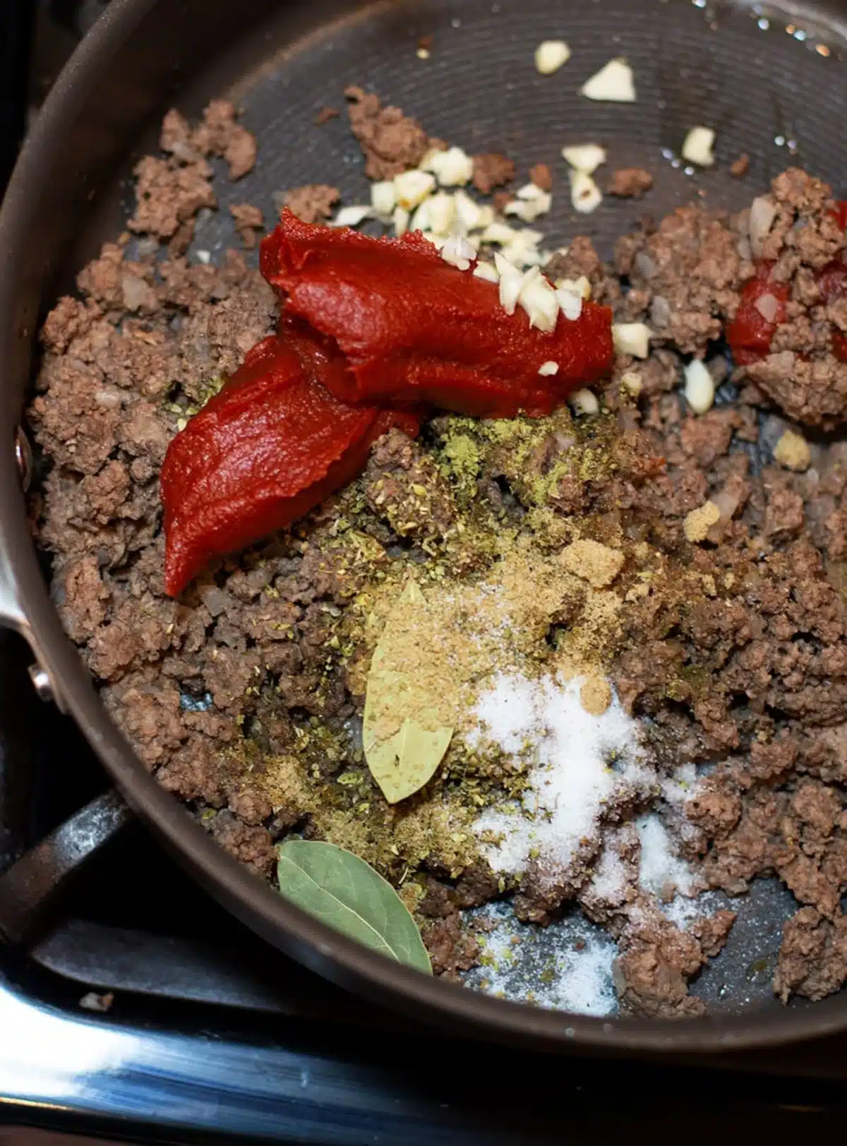 Skillet filled with ground beef, tomato paste, and onions.