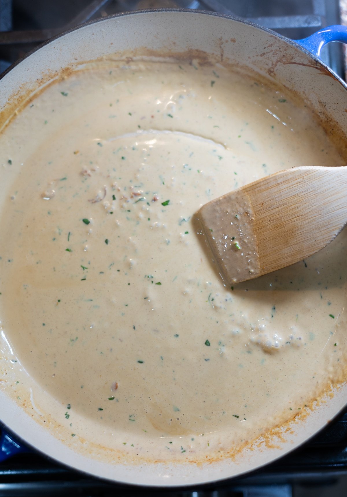 Person stirring alfredo sauce in a saucepan. 