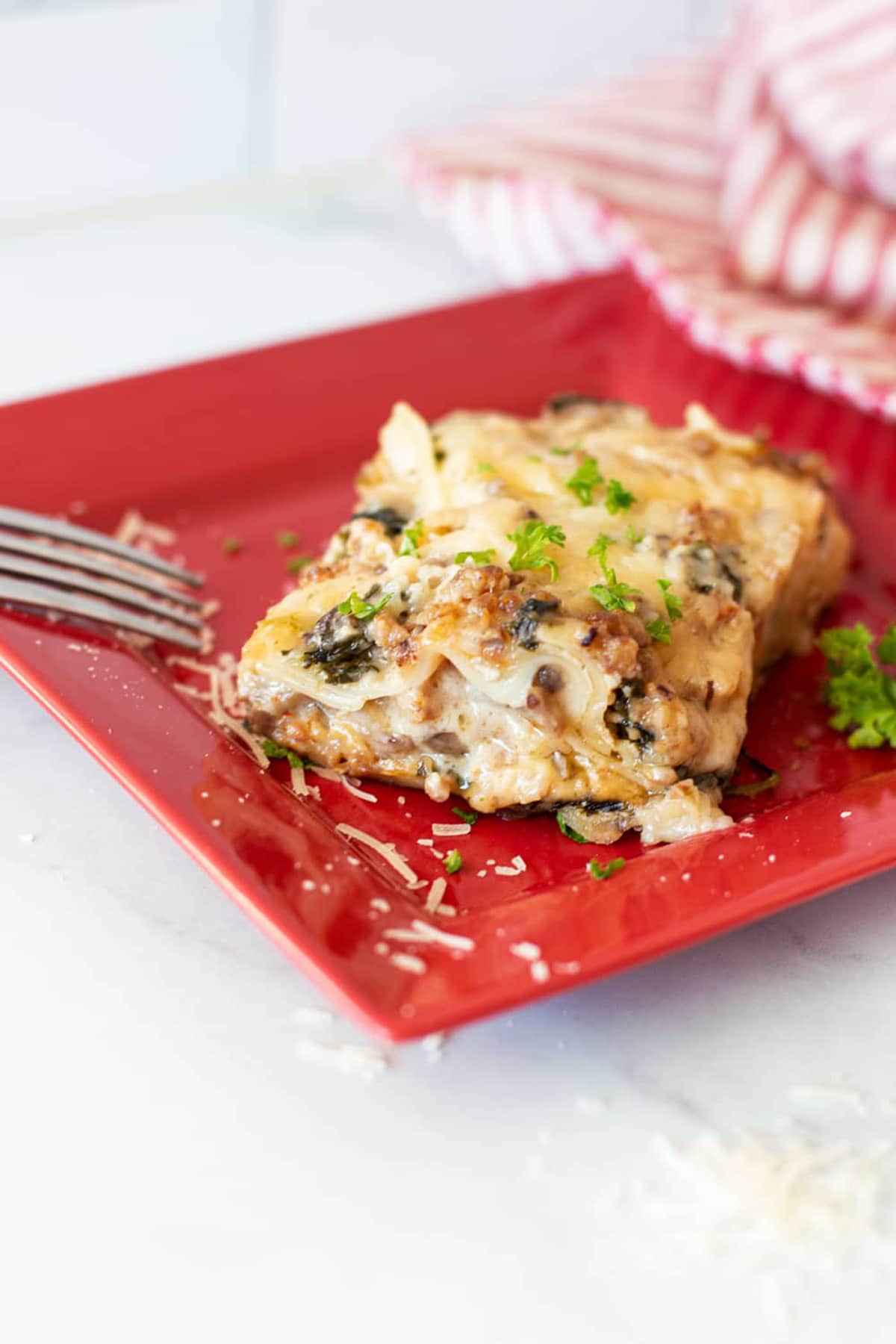 Piece of white laagna on a red plate, fork on side. 