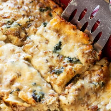 Person using a spatula to serve a piece of white lasagna.