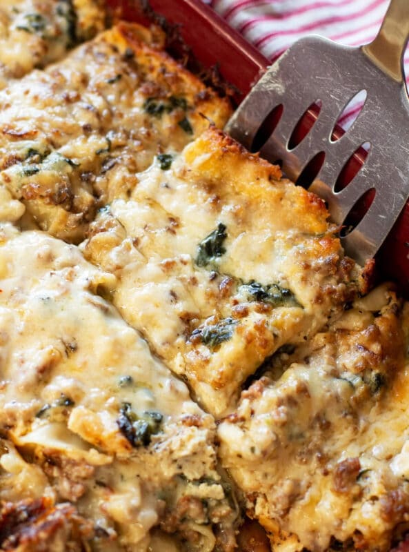 Person serving a piece of white sauce lasagna from a baking dish.