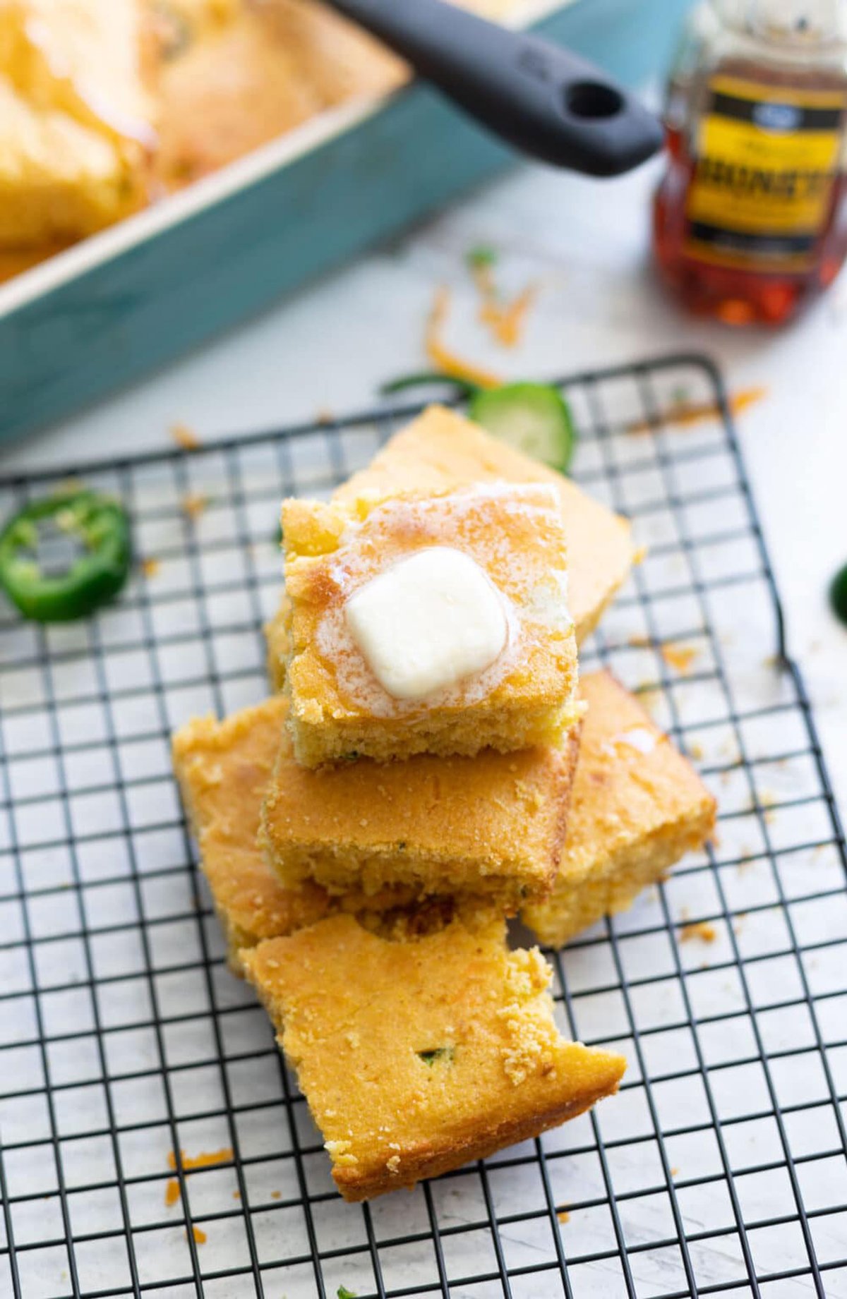 Stacked pieces of cornbread on a cooling rack topped with butter.