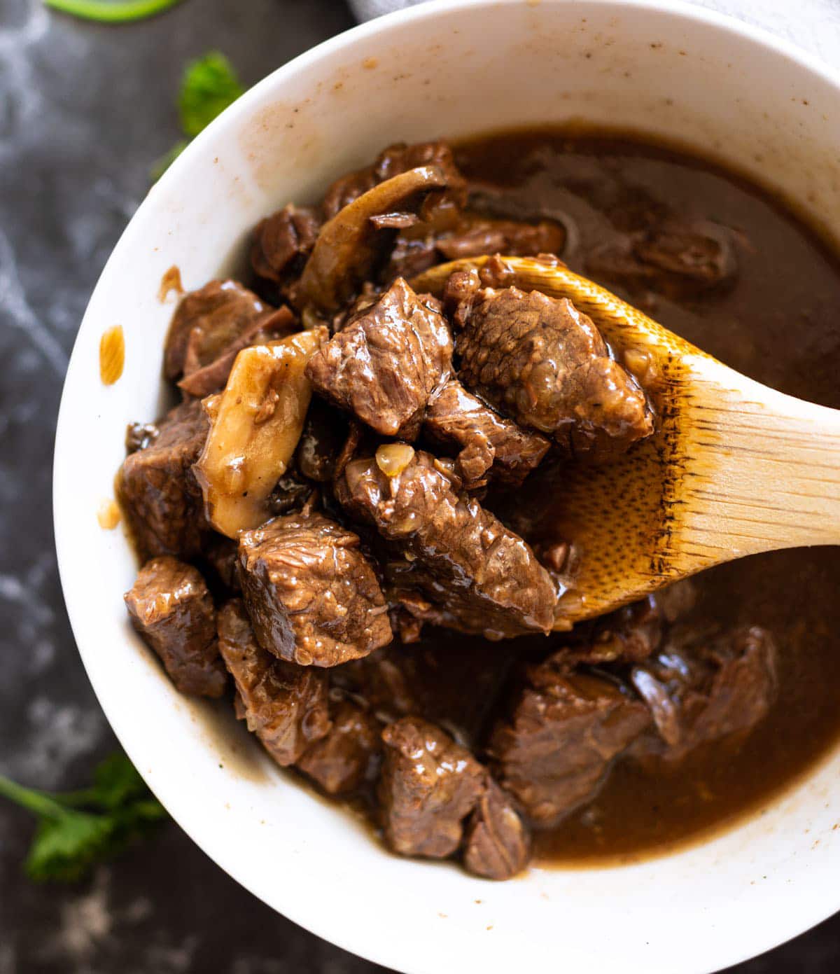 Person using a wooden spoon to show cooked beef tips. 