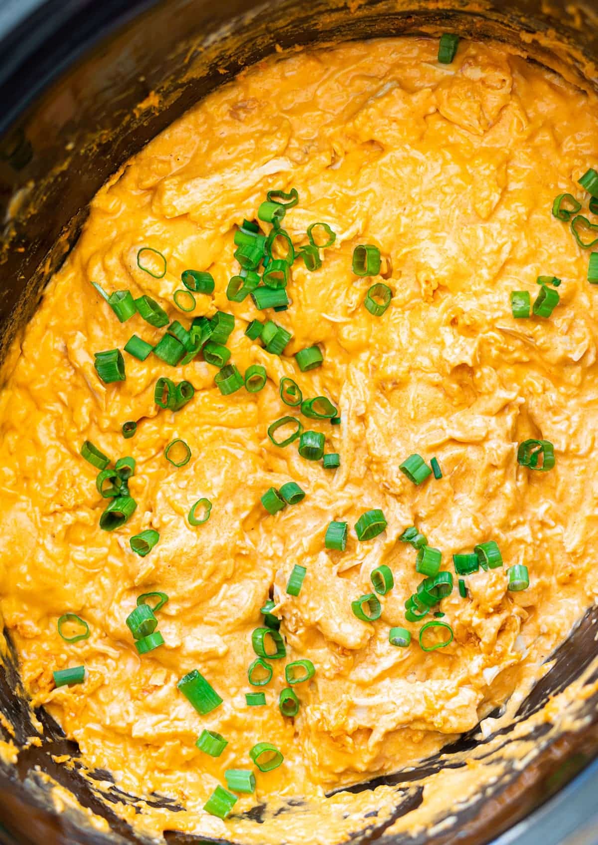 Buffalo chicken dip in a crock pot topped with scallions. 