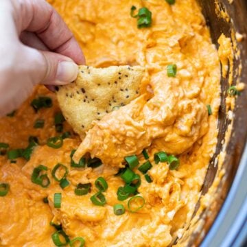 Chip being dipped into the chicken buffalo dip in a crock pot.