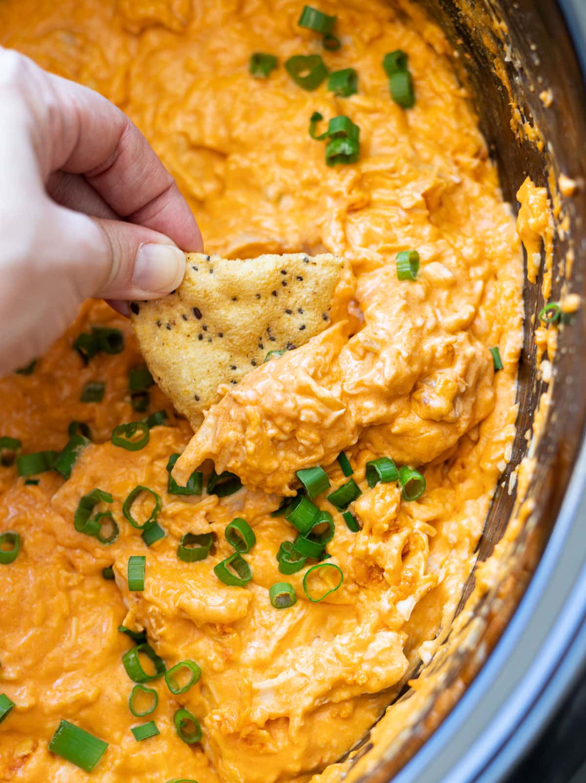 Person dipping a chip into buffalo chicken dip in a crock pot.