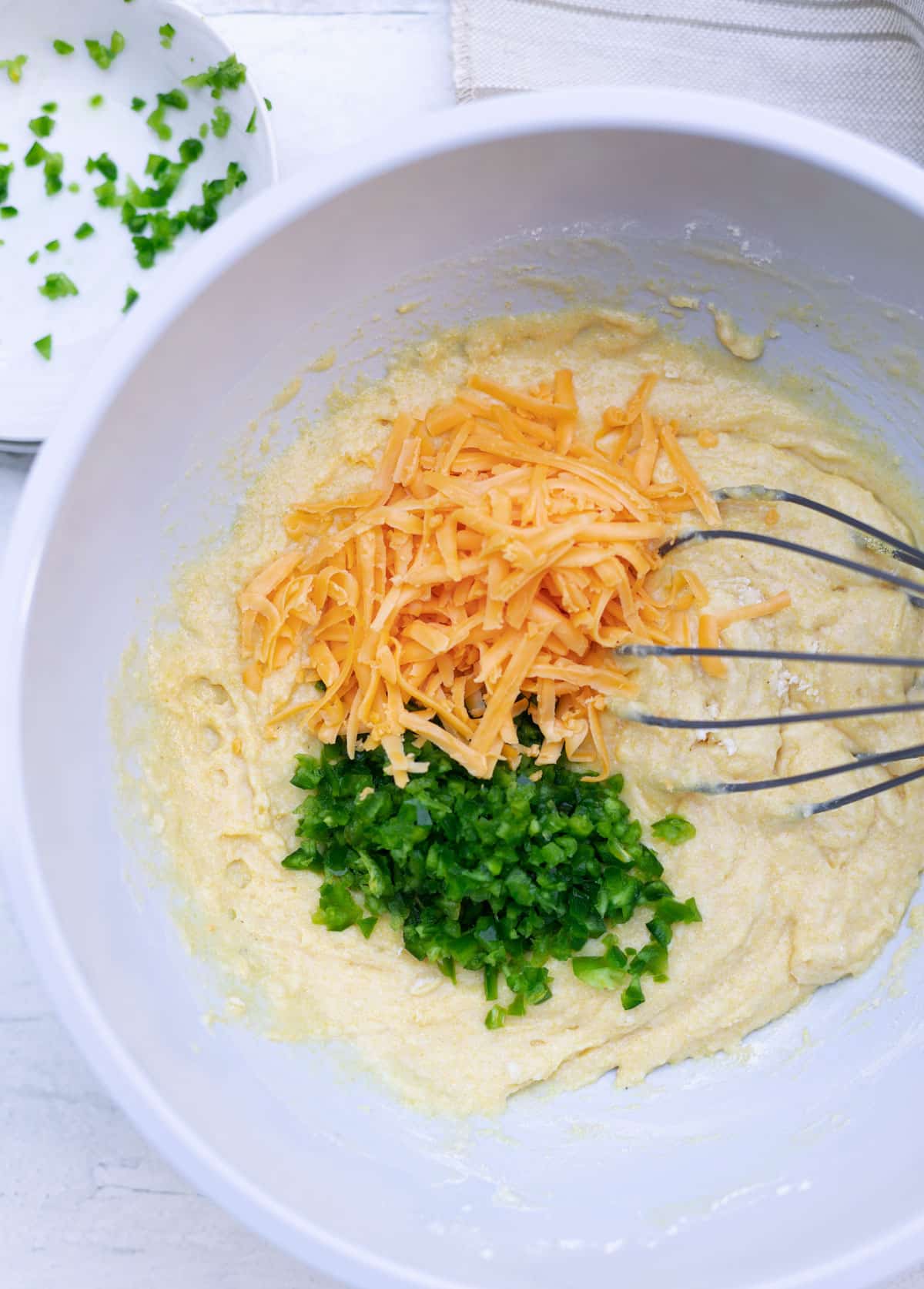 Large bowl filled with shredded cheese, diced jalapeno peppers, and cornbread batter. 