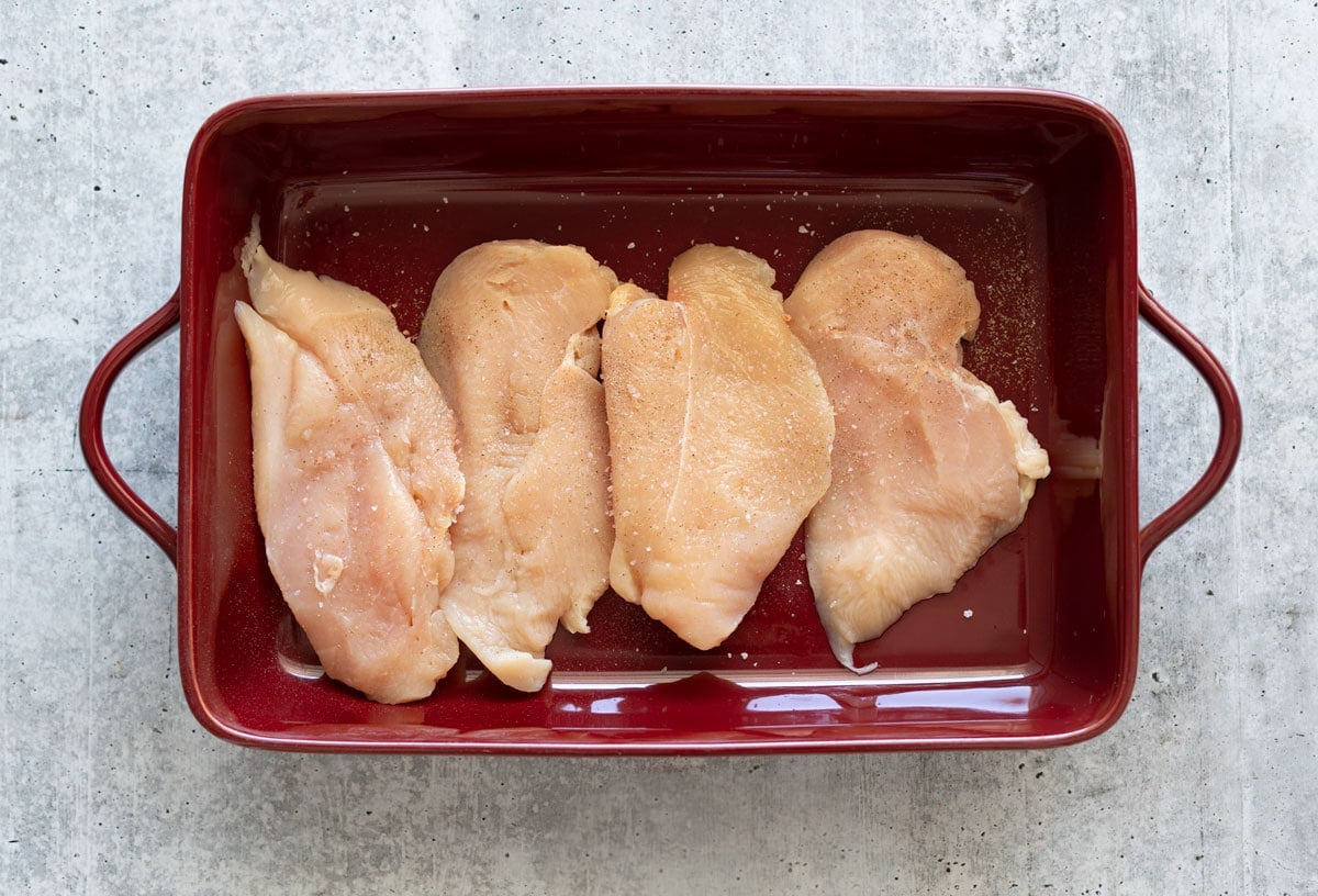 4 raw chicken breasts in a baking dish getting ready top be baked. 
