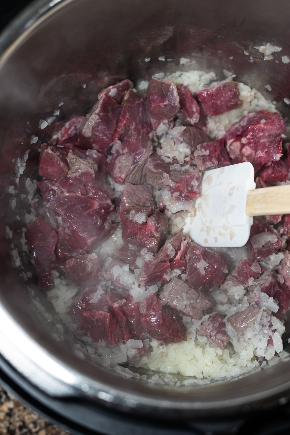 Person cooking beef stew meat win with onions and garlic in the Instant Pot. 