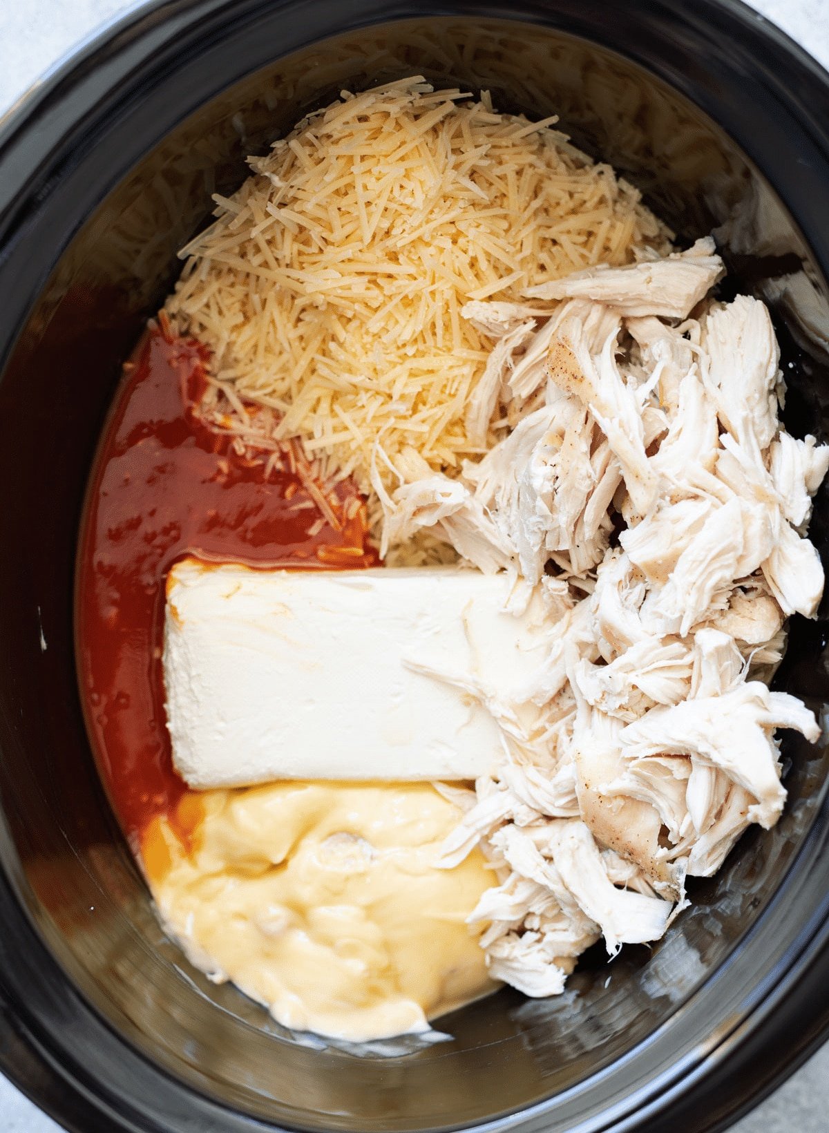 Ingredients in a crock pot to make buffalo chicken dip. 