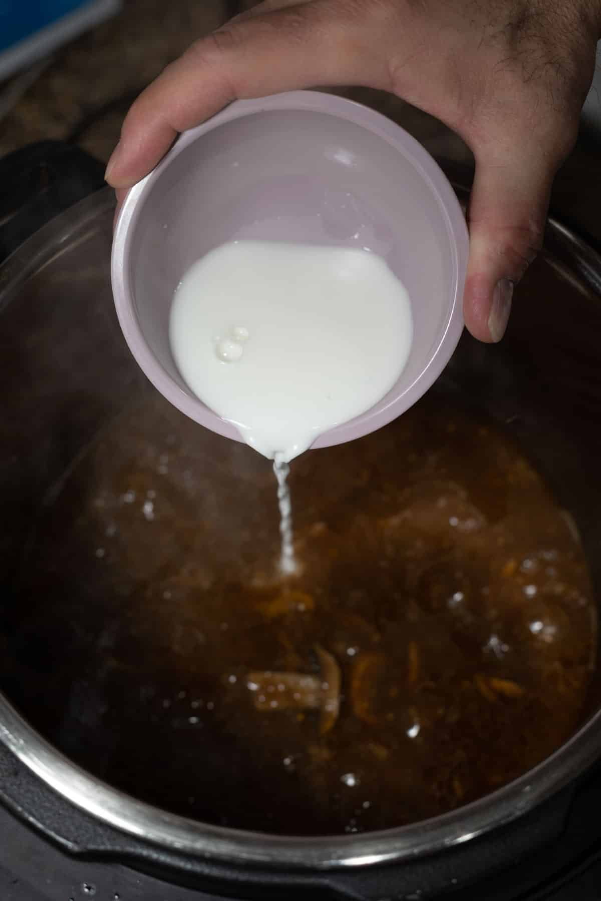Person pouring a cornstarch slurry into an Instant Pot with beef tips.