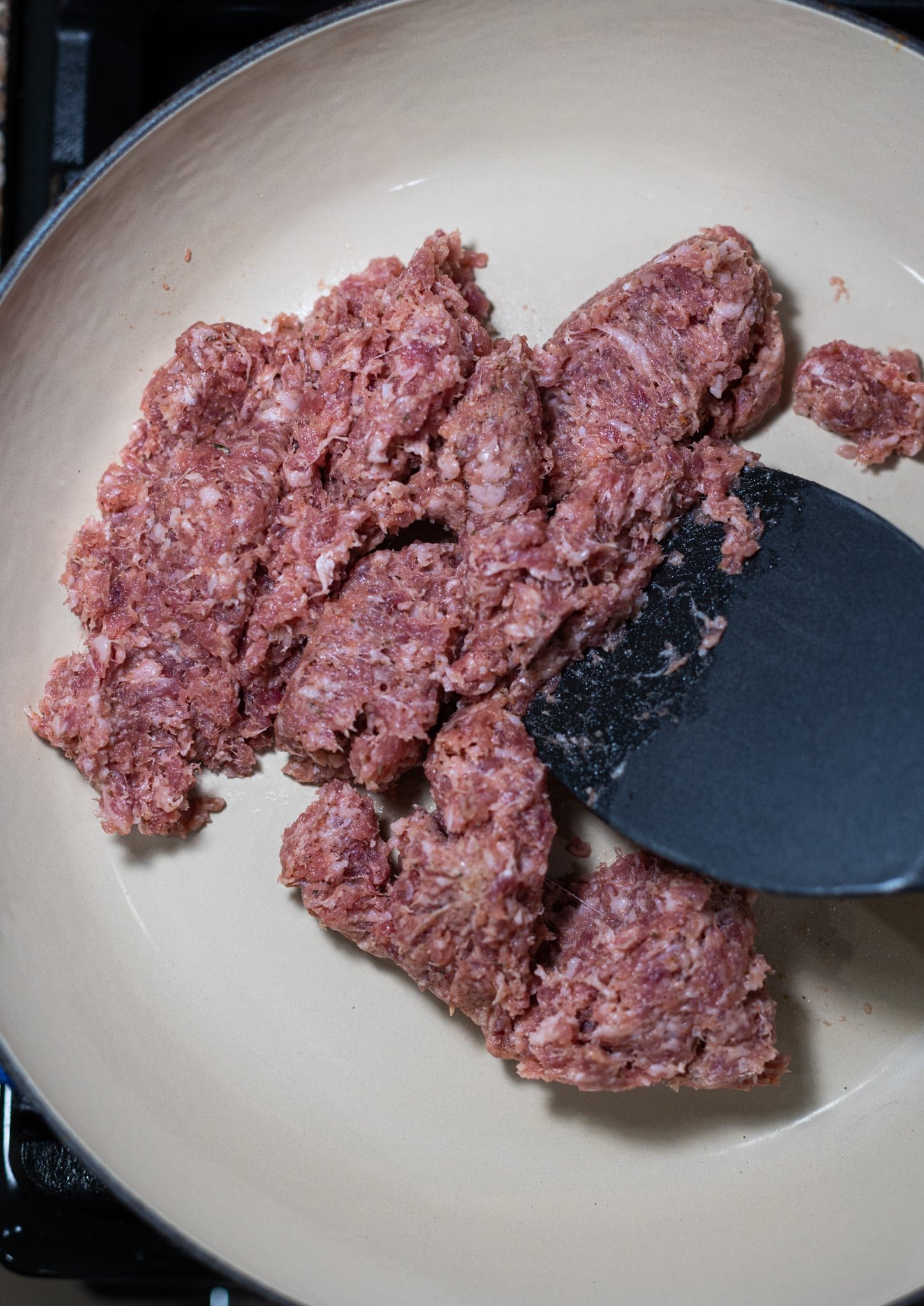 Person. browning sausage in a skillet.