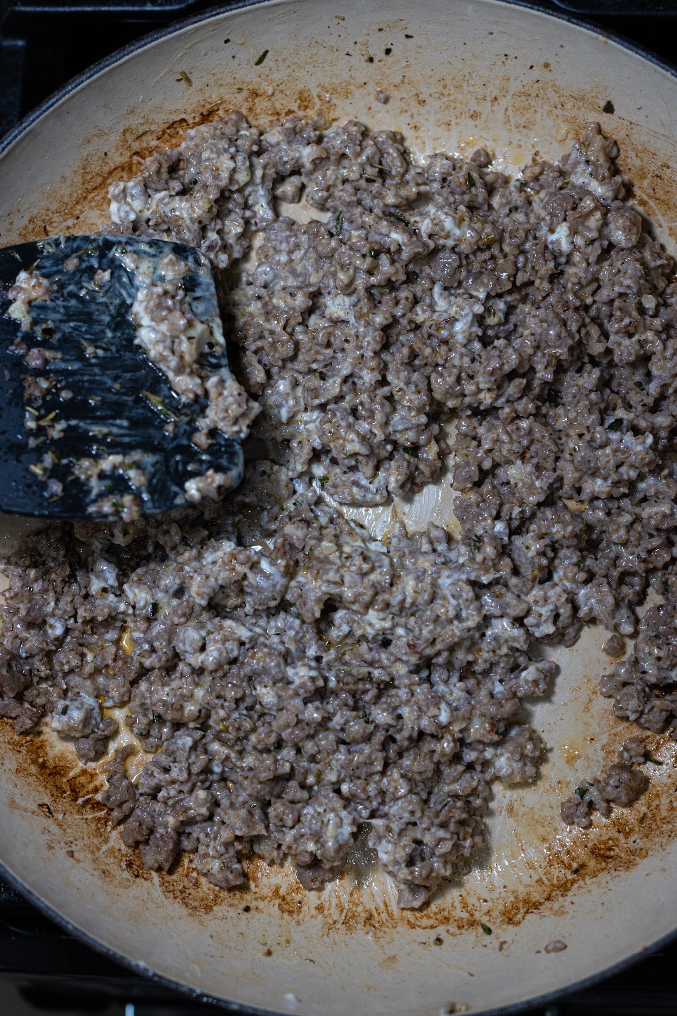 Person mixing together cream cheese in a skillet with sausage. 