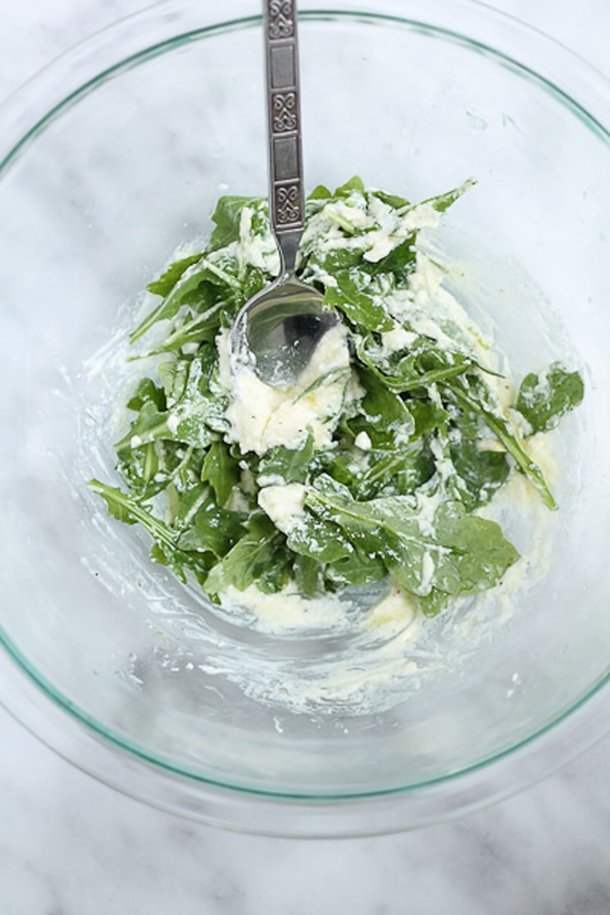 Glass bowl filled with aragula and goat cheese with lemon. 