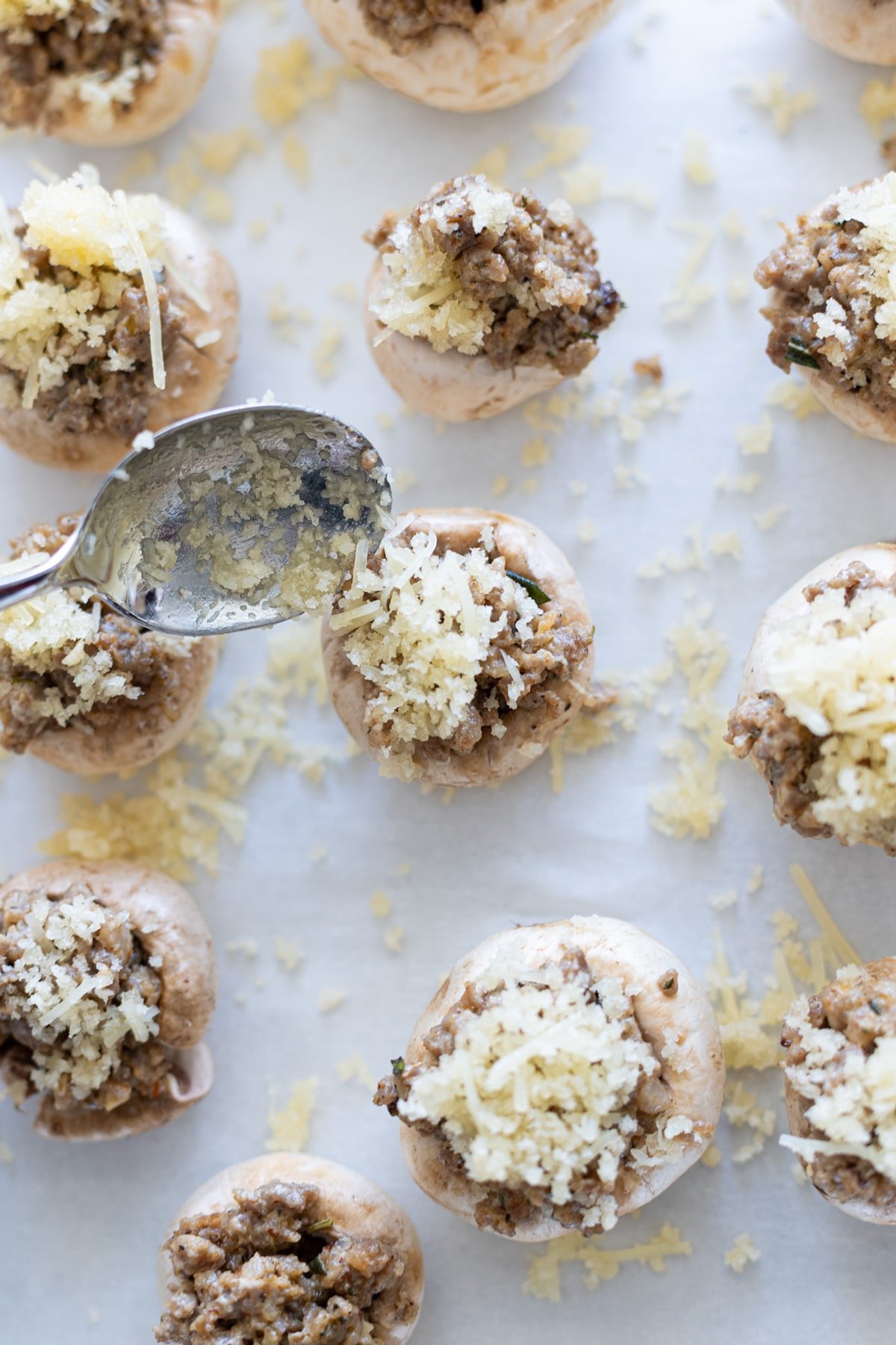 Person adding a topping to the stuffed mushrooms.