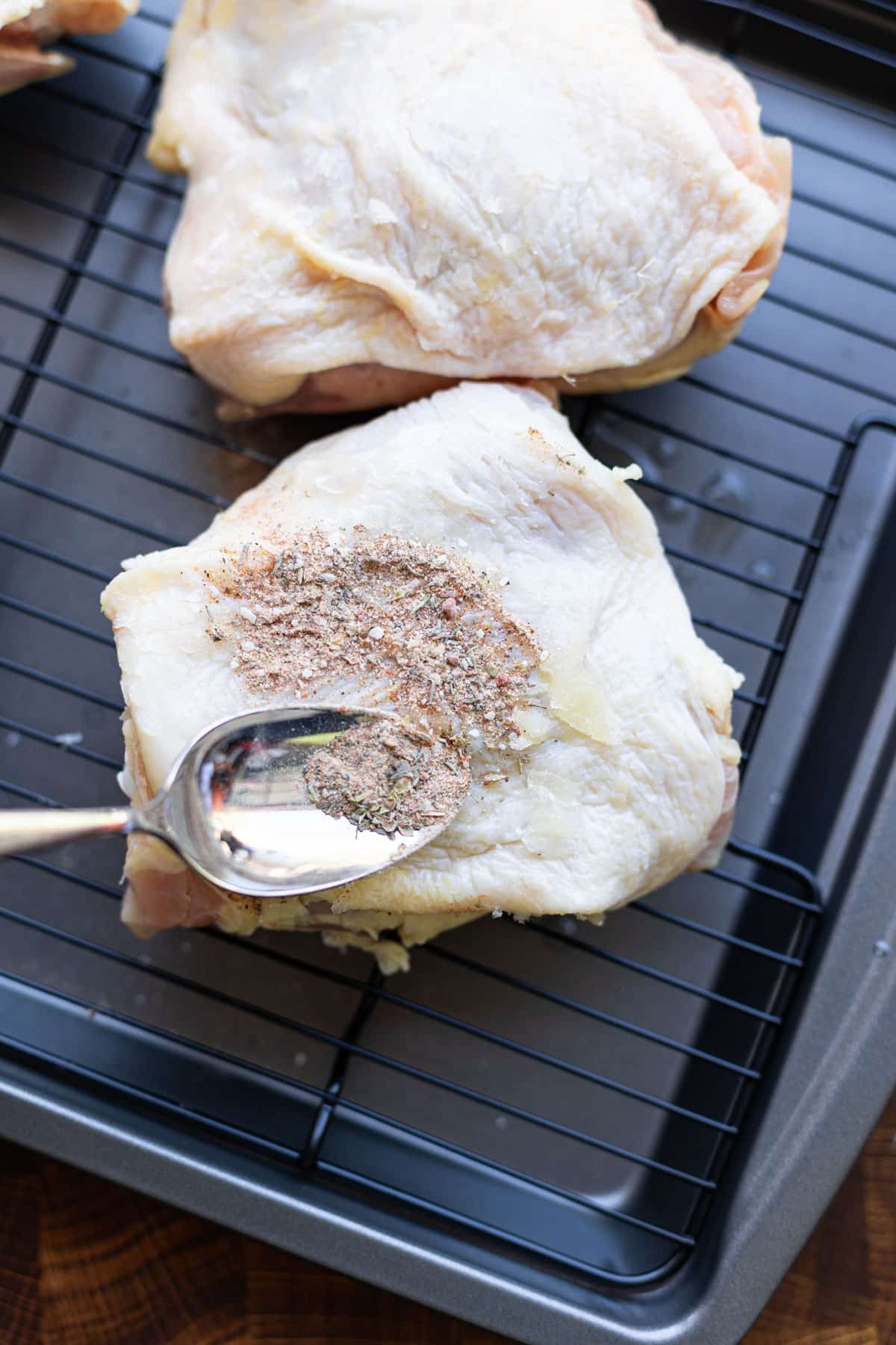 Person adding seasoning to raw chicken thighs. 