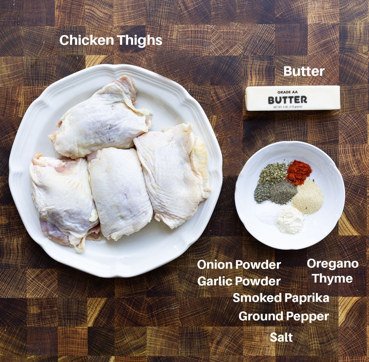 Plate filled with chicken thighs, butter, and a lot of seasonings on a counter top.