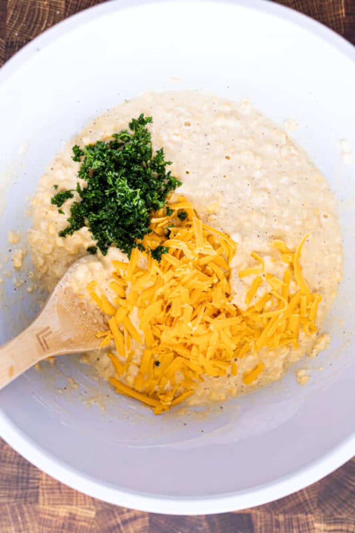 White bowl containing person stirring corn fritter ingredients. 