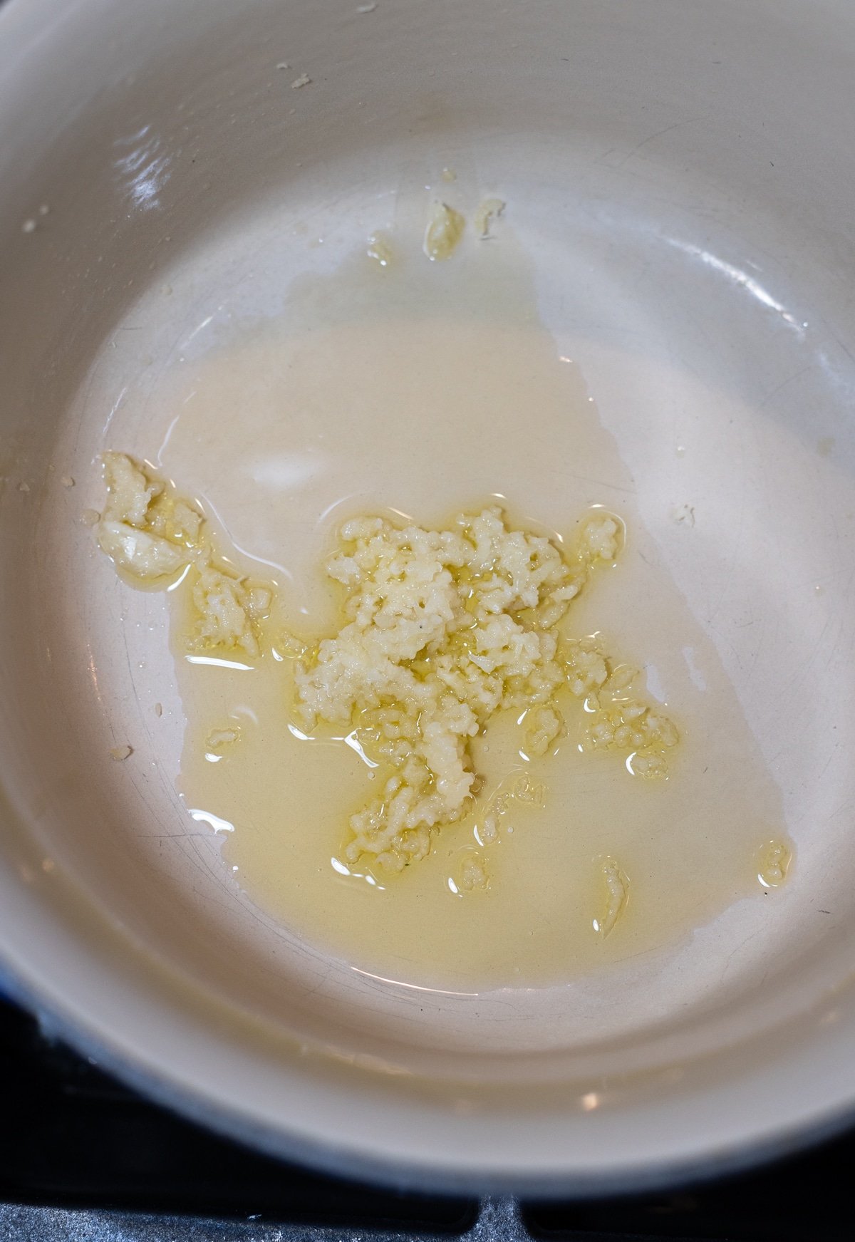 Fresh garlic being sautéed in a pot on the stove with olive oil. 