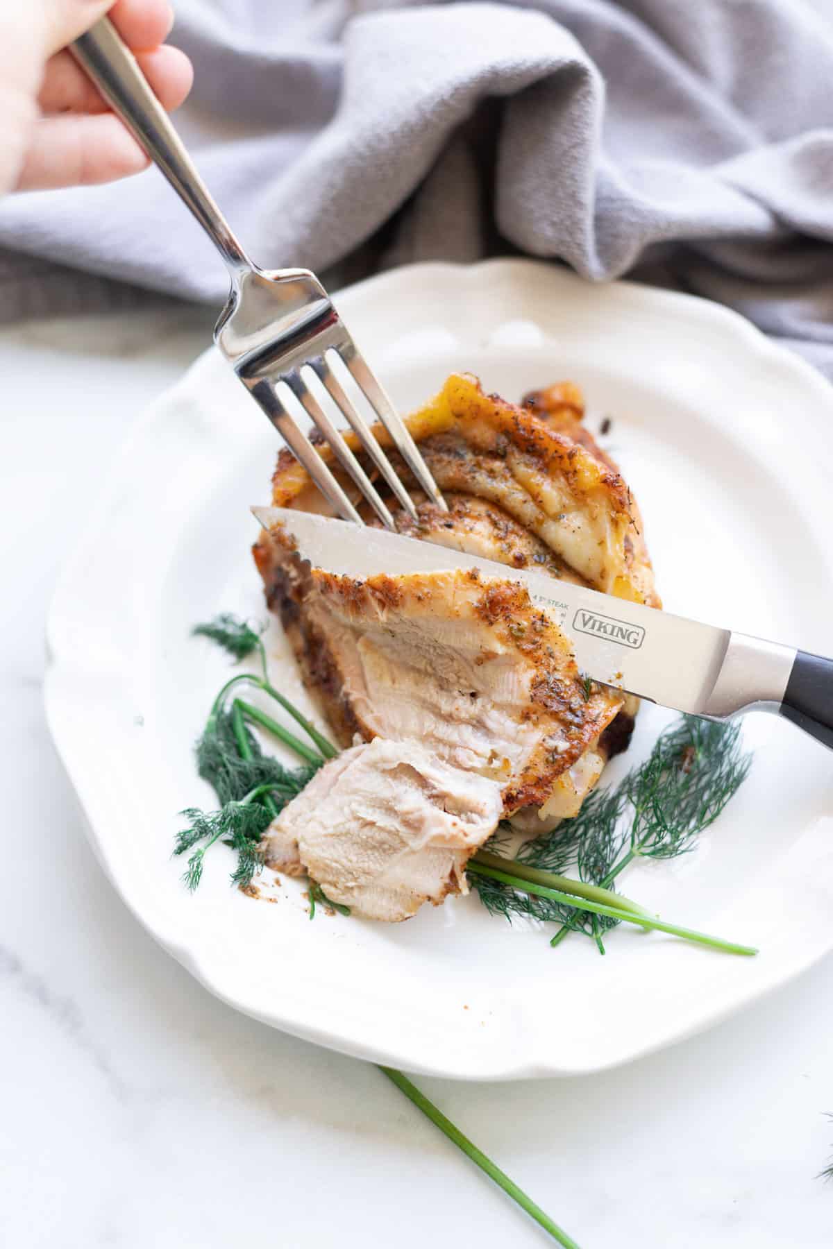 Person cutting chicken thighs with a knife and fork.