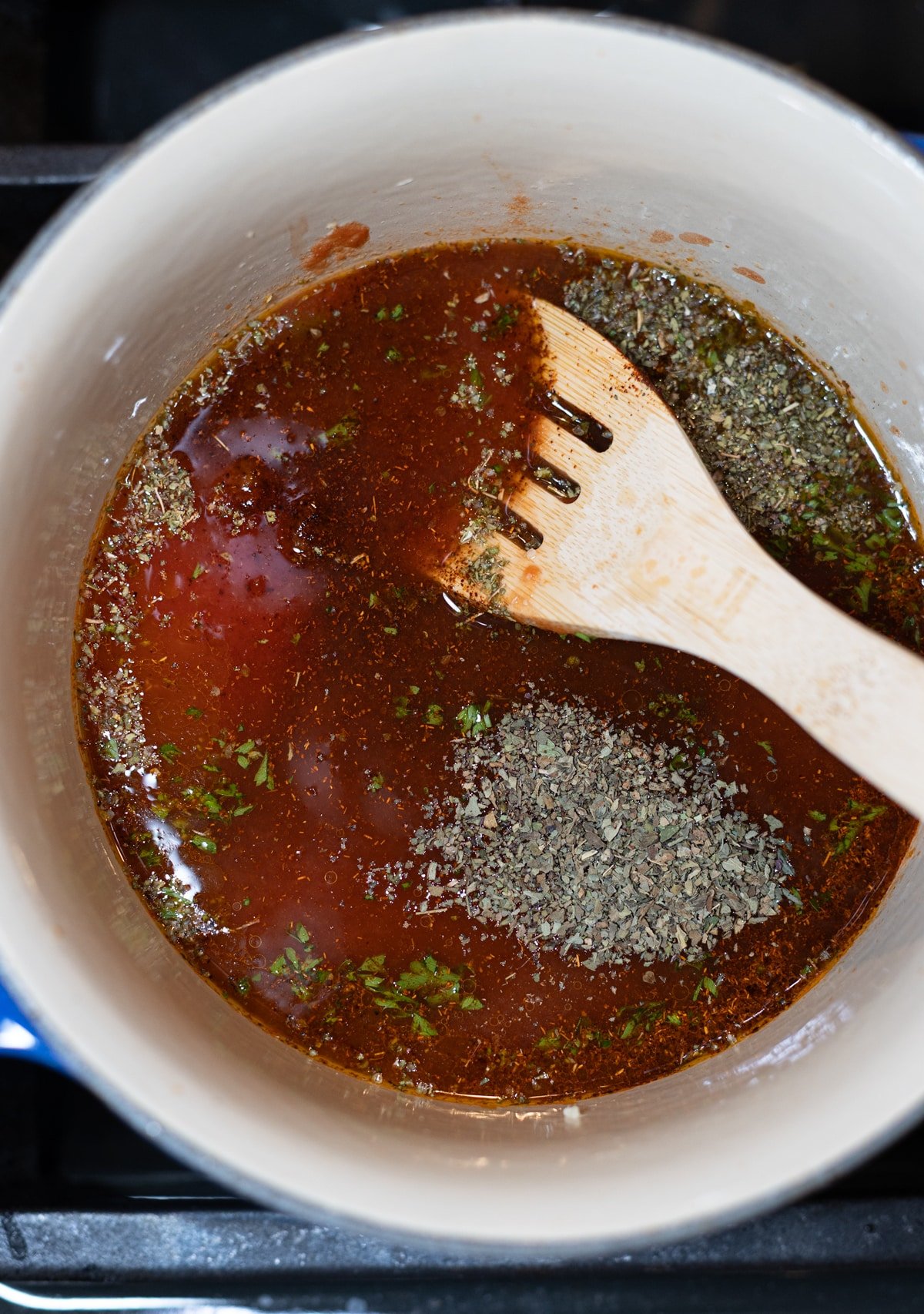 Person adding herbs to a pan that has the tomato sauce and water.