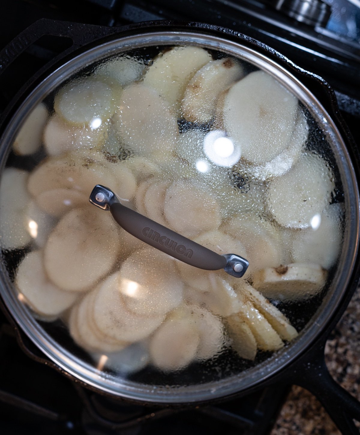 Person covering a skillet filled with fried potatoes.
