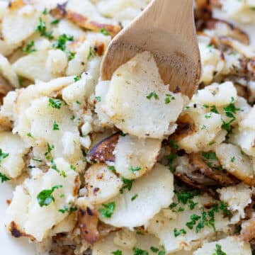 Skillet potatoes being served with a spoon.