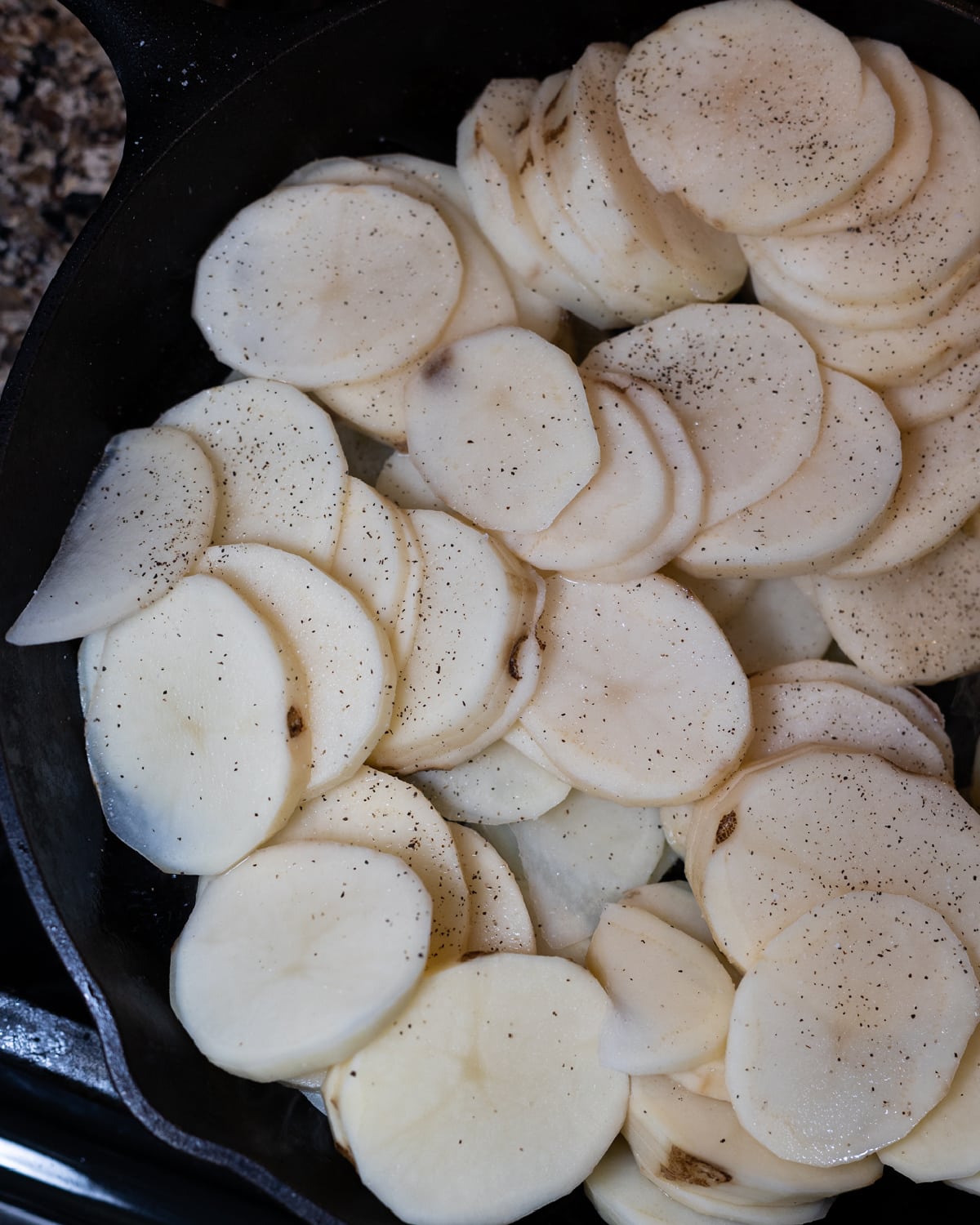 Person seasoning potatoes with salt and pepper before frying.
