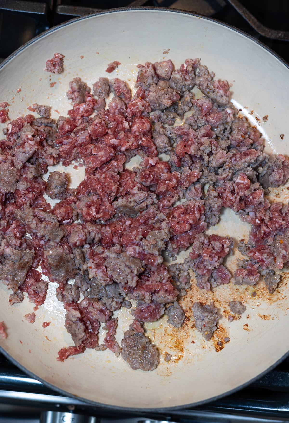 Person browning ground sausage in a skillet. 