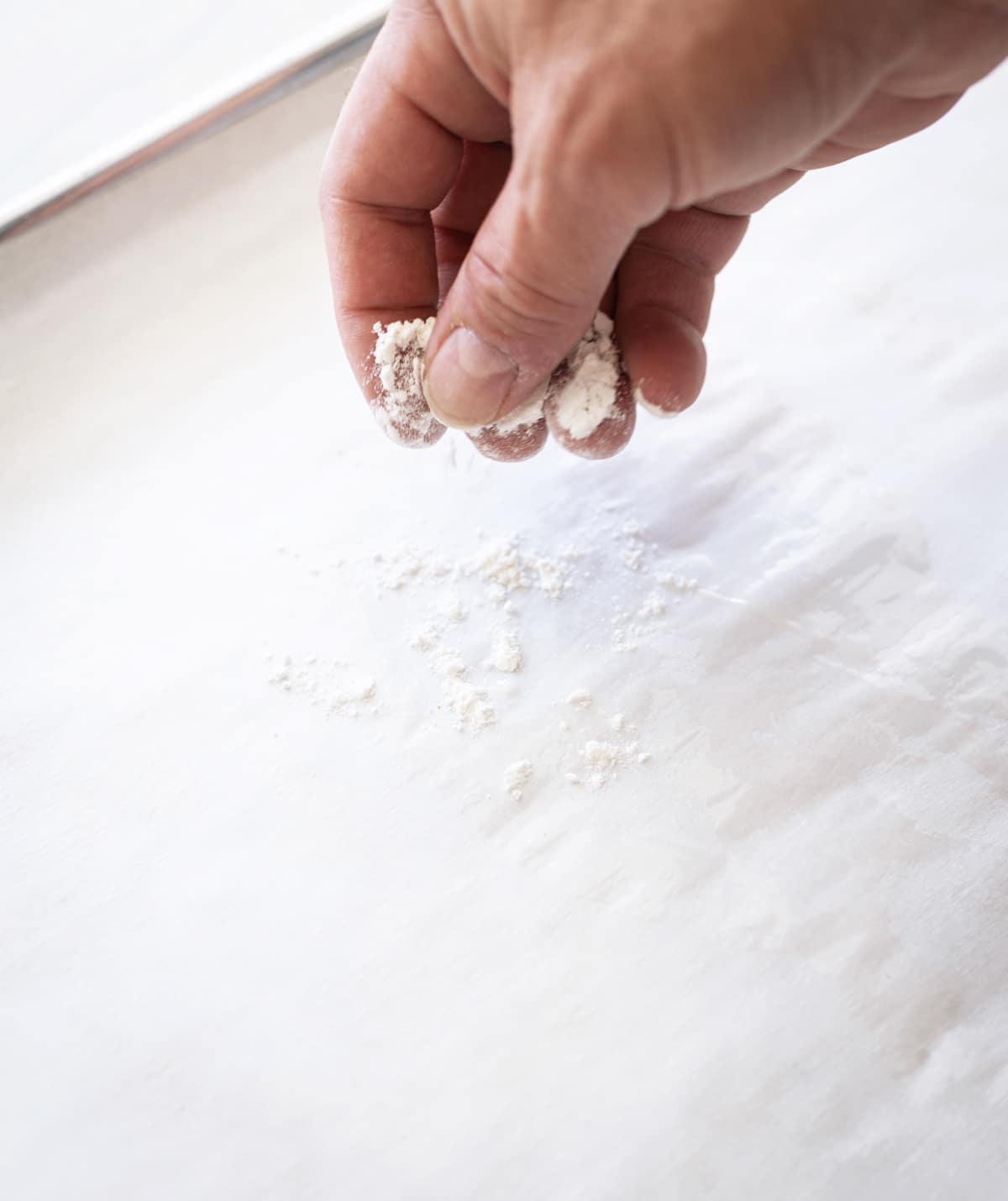 Person sprinkling a pinch of flour on a cookie sheet. 