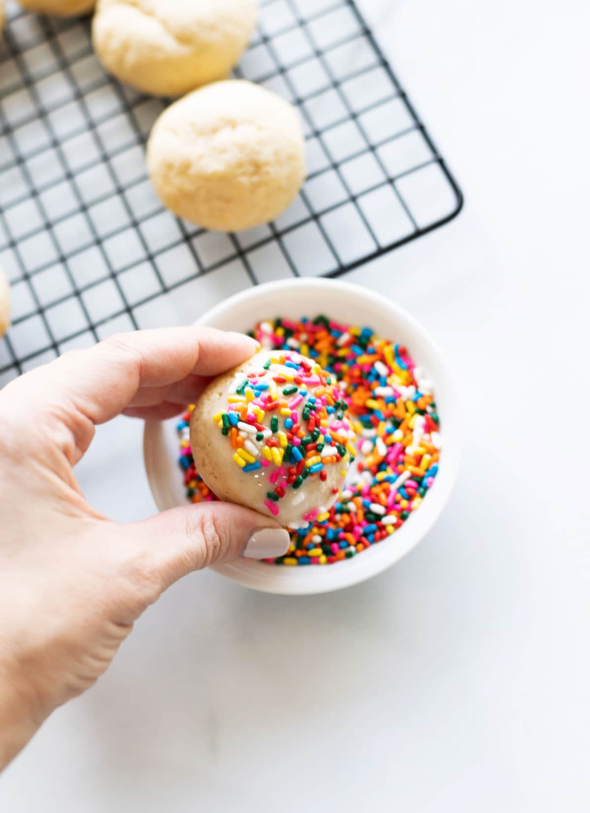 Person dipping an anise cookie into sprinkles. 