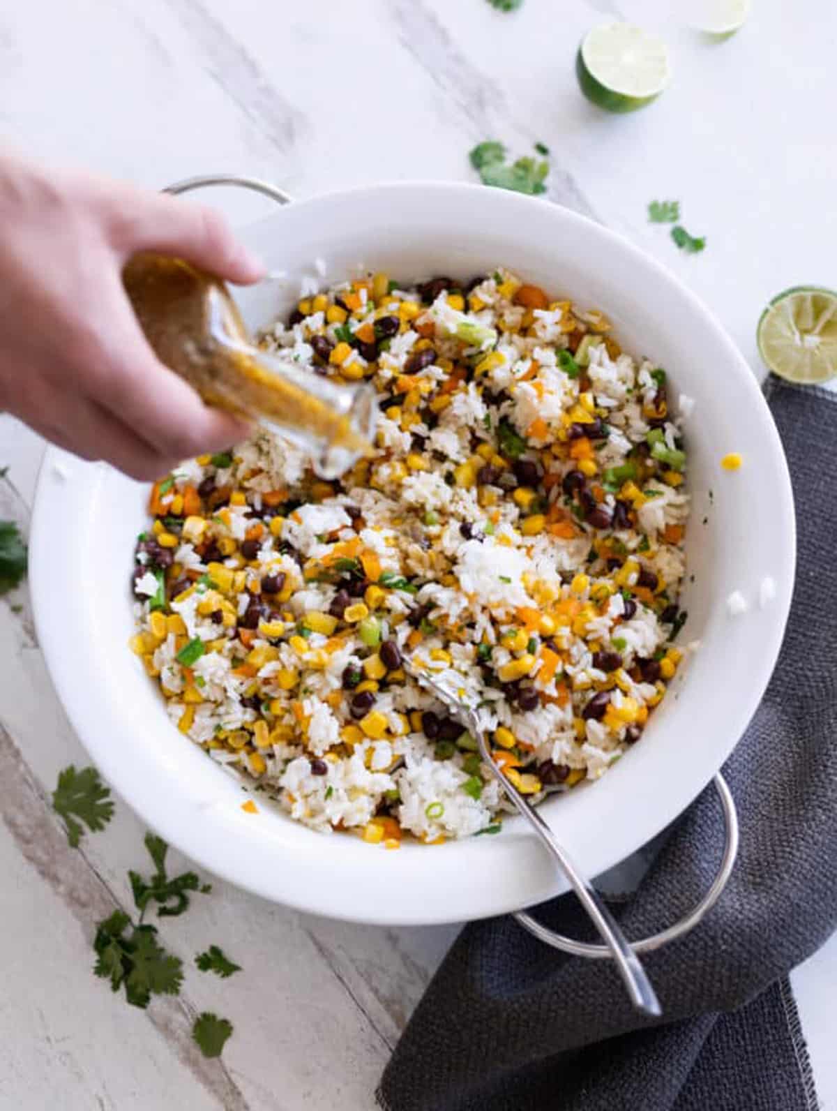 Person pouring dressing in a corn and black bean salad.