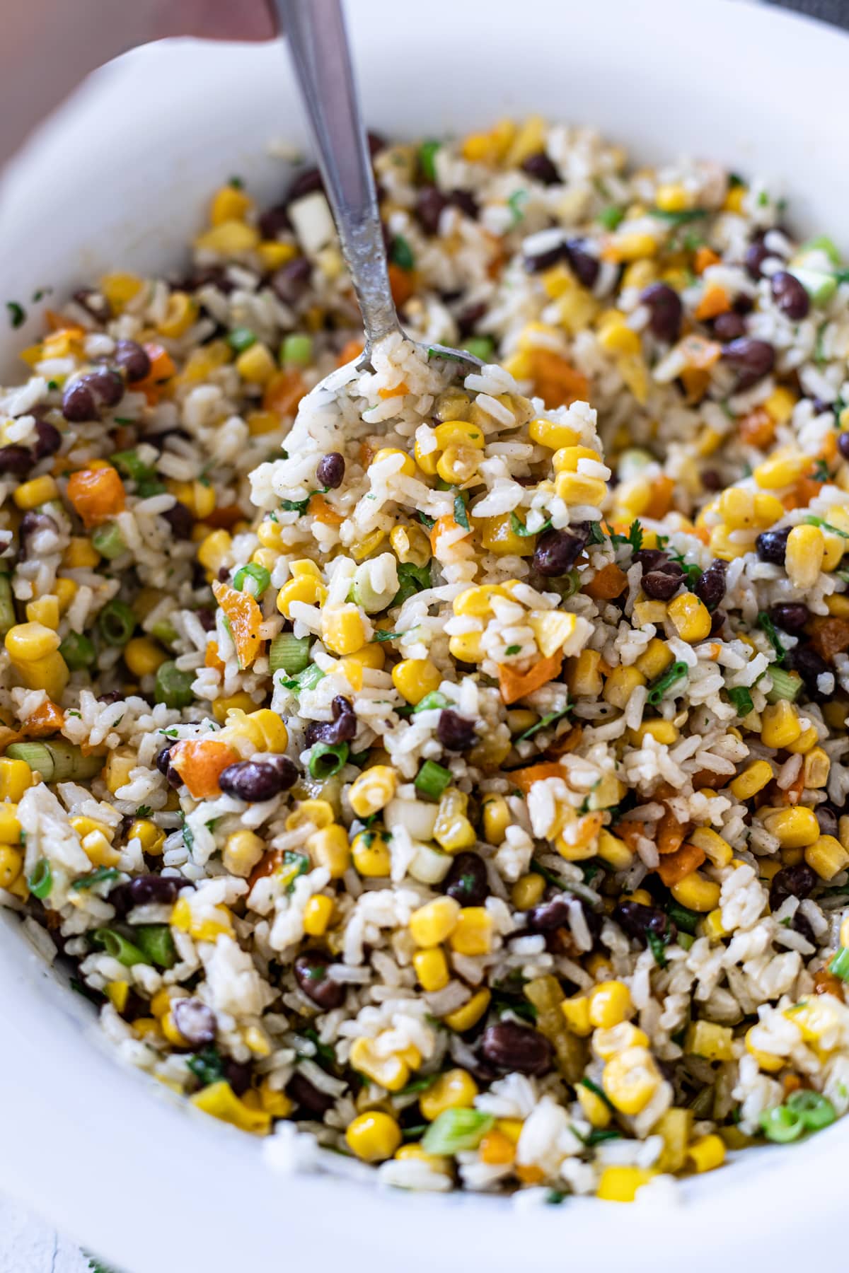 Close up of a person serving corn and black bean salad with a spoon.