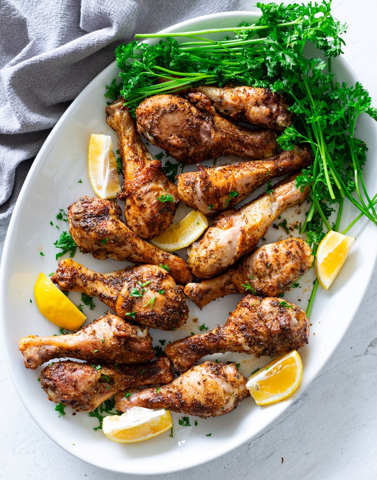 Large white platter filled with drumsticks topped with seasonings that are freshly baked.